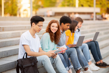 Students sitting on stairs on campus with laptops